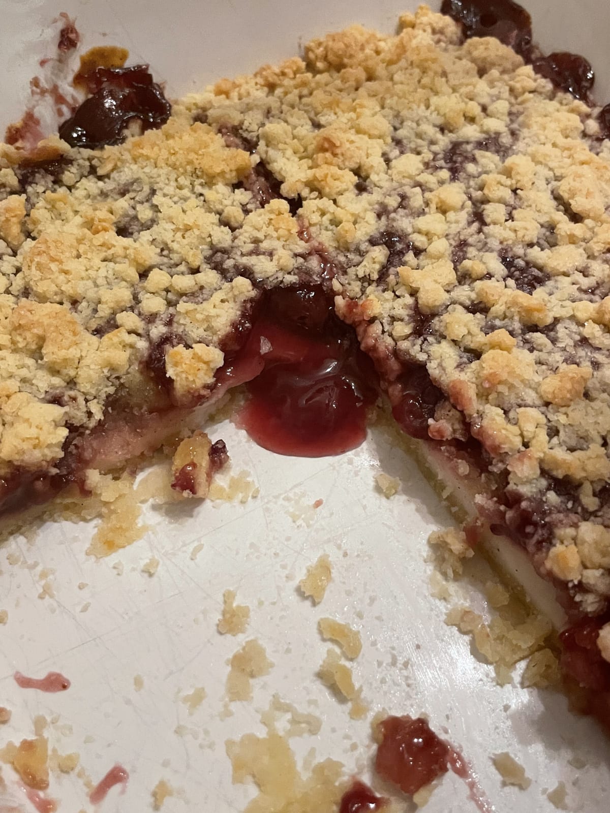 Ein Bild von einem Kuchen, aus dem etwas Kirschsosse rausläuft. Helle crumbles oben auf dem Kuchen.