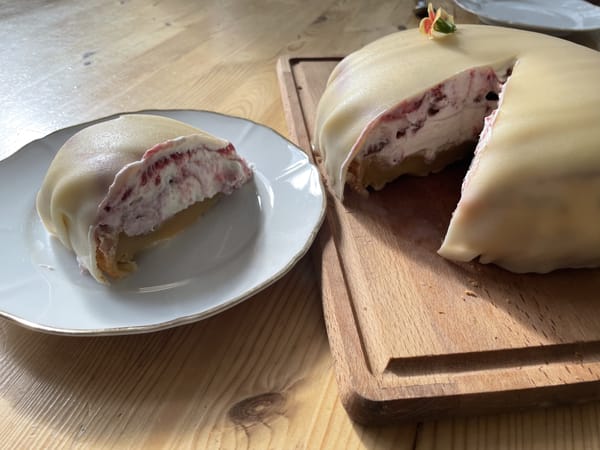 Ein aufgeschnittener Sahnekuchen mit Marzipan bezogen. Ein Kuchenstück ist auf einem weißen Teller gelegt. Daneben steht der Kuchen.