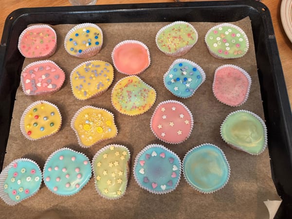 Ein Bild von 19 farbigen muffins, mit verschiedenen Streuseln und Farben auf einem Backblech. Ein lustiger anblick.