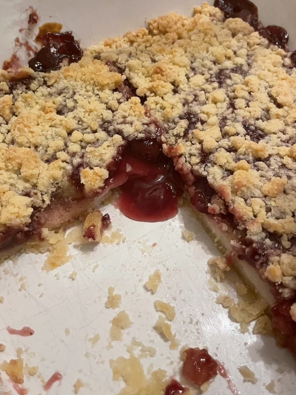 Ein Bild von einem Kuchen, aus dem etwas Kirschsosse rausläuft. Helle crumbles oben auf dem Kuchen.